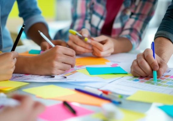 Active class participation is evident in the image with students using colorful sticky notes and writing instruments during a collaborative session